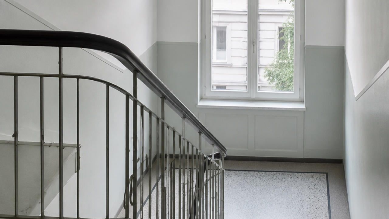 Treppenhaus-Podest in einem Altbau mit geschwungenem Geländer, hohem Fenster und Terrazzoboden